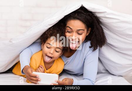 Joyeuse mère et fille jouant aux jeux mobiles allongé dans le lit Banque D'Images