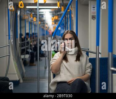 Fille parle sur téléphone portable à l'intérieur d'un train de métro vide. Une belle femme touristique d'apparence se trouve dans la voiture de métro. Portrait de la femme passager à l'aide d'un téléphone portable. Banque D'Images