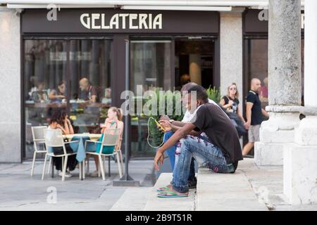 CRÈMES, ITALIE - 2 SEPTEMBRE 2015 : deux hommes noirs s'assoient sur les marches du bâtiment avec un téléphone dans les mains. Cremona. Italie Banque D'Images