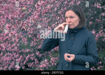 Femme utilisant un jet nasal à l'extérieur pour le traitement d'allergie au pollen d'arbre Banque D'Images