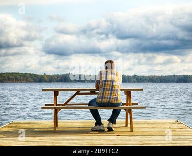 Homme assis sur un banc devant un lac Banque D'Images