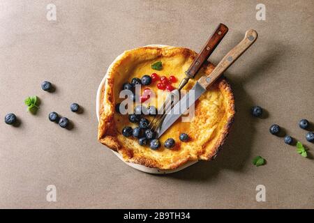 Fresh baked Dutch pancake bébé dans une plaque en céramique servi avec blackberry et baies de groseille rouge, bol de miel, vintage couverts sur fond beige. Banque D'Images