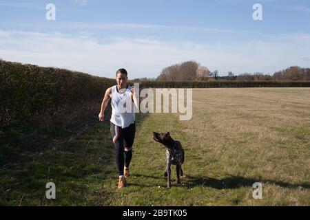 Une femme qui fait du jogging avec son chien animal de compagnie, un petit pointeur à poil court allemand Banque D'Images