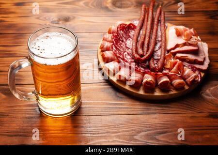 Tasse de bière et assortiment d'en-cas sur une table en bois. Saucisse, salami, jambon, bacon. En-cas salés à la bière, chips, noix de wasabi, arachides salées, croutons. Banque D'Images