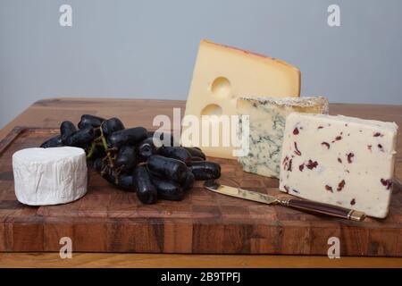 Wensleydale, Stilton, Jarlsberg et fromage de chèvre avec de longs raisins noirs sur une planche à découper Banque D'Images