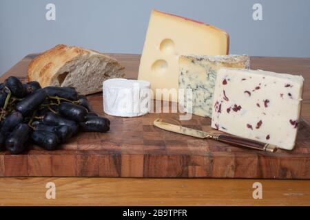 Levain avec Wensleydale, Stilton, Jarlsberg et fromage de chèvre avec de longs raisins noirs sur une planche à découper Banque D'Images