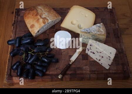 Levain avec Wensleydale, Stilton, Jarlsberg et fromage de chèvre avec de longs raisins noirs sur une planche à découper Banque D'Images