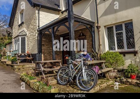 Un cycliste se reposant et prenant une pause devant le pub durant Arms à Ashsprington dans la vallée de Dart, South Hams, Devon, Royaume-Uni. Mars 2018. Banque D'Images