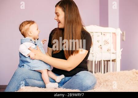 Maman joue avec sa fille de nouveau-né dans la chambre. Rire et joie. Le concept de famille, de maternité et de garde d'enfants. Banque D'Images