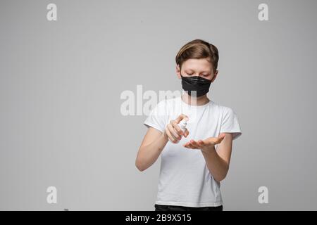 Garçon en masque noir vaporisant antiseptique. Concept d'arrêt des virus. Banque D'Images