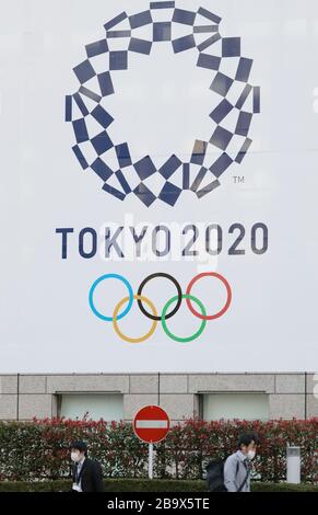 Tokyo, Japon. 25 mars 2020. Les piétons portant des masques se promenent devant une affiche de l'emblème de Tokyo 2020 située devant l'édifice du gouvernement métropolitain de Tokyo à Tokyo, au Japon, le 25 mars 2020. Le ministère japonais de la santé et les gouvernements locaux ont déclaré mercredi que 41 nouvelles infections à COVID-19 avaient été confirmées à Tokyo, tandis que 66 nouveaux cas avaient été confirmés par 12 autres autorités locales, ce qui porte le nombre total de personnes infectées au Japon à 1 277 à 20 h, heure locale. Crédit: Du Xiaoyi/Xinhua/Alay Live News Banque D'Images