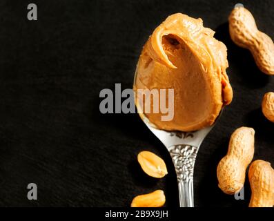 Beurre d'arachide dans la cuillère sur fond noir Banque D'Images