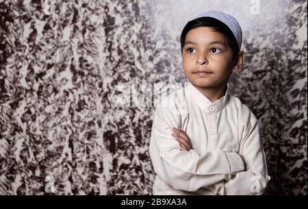 Portrait d'enfant musulman avec casquette musulmane et robe ethnique blanche donnant l'expression vers la lumière Banque D'Images