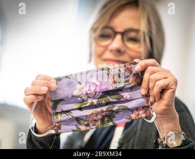 24 mars 2020, Hessen, Francfort-sur-le-Main: Kerstin Jentschke de la "Cariteam" de Caritas Francfort montre son masque de visage fini. Pour le moment, elle et ses collègues sont à coudre les masques bobinables faits de tissus de coton colorés eux-mêmes. Ces masques sont nécessaires de toute urgence pour les soins aux personnes âgées, par exemple. Normalement, le Cariteam offre aux chômeurs de longue durée, aux demandeurs d'asile ou aux réfugiés la possibilité d'acquérir une expérience professionnelle. Photo: Frank Rumpenhorst/dpa Banque D'Images