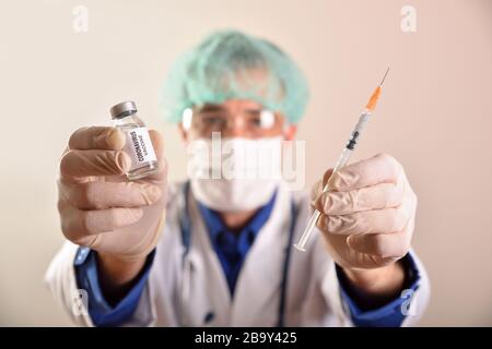 Médecin avec flacon de vaccin contre le virus covid-19 et seringue dans ses mains avec protection du visage et des mains sur fond brun isolé Banque D'Images
