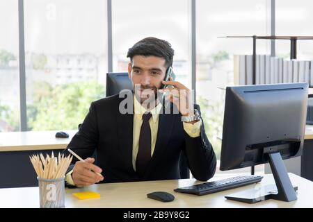 Un homme d'affaires dans un costume bien habillé assis au téléphone avec un sourire vif dans le bureau Banque D'Images