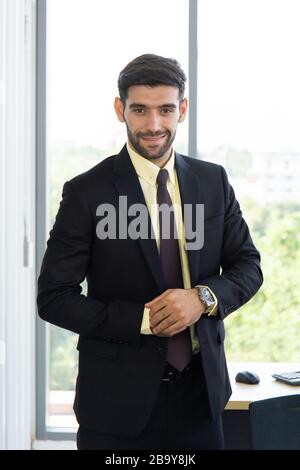 Un homme d'affaires dans un costume bien habillé debout dans le bureau avec un sourire brillant Banque D'Images