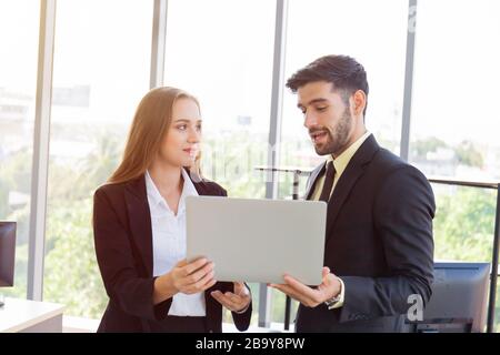 Deux hommes et femmes d'affaires étaient habilement vêtus d'un costume et se sont réunis debout à côté du mur de verre au bureau. Banque D'Images