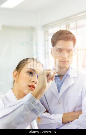 De plus près, un groupe de scientifiques, de jeunes femmes et de jeunes hommes enregistrent des formules sur une planche de verre et ont une belle lumière orange. Banque D'Images