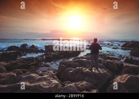 Seascape le soir. La côte rocheuse. Silhouette d'un homme sur la plage qui regarde le coucher de soleil magique Banque D'Images