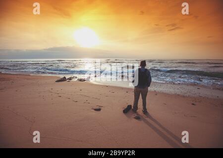 Seascape le soir. Plage de sable. Silhouette de l'homme sur la plage en regardant le coucher de soleil magique Banque D'Images