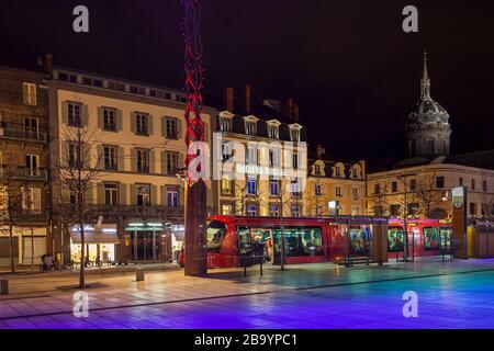 Vue nocturne sur la place de Jaude à Clermont Ferrand, France, avec tramway rouge sur la gare, lumières de la ville et église Saint Pierre des mineurs Banque D'Images