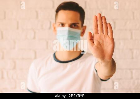 Jeune homme en bonne santé dans un masque de protection médicale sur le visage montrant un geste d'arrêt avec sa paume. Arrêter les virus et les maladies épidémiques contagieuses. Méa préventive Banque D'Images