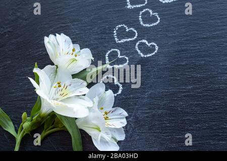 Contexte avec des fleurs d'Alstroemeria blanches ou un lys péruvien ou Lily des Incas avec des coeurs dessinés sur une tuile noire Banque D'Images
