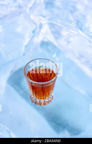 Un verre de whisky se tient sur de la glace dépolie. Vue de dessus du côté. Pour la publicité d'une boisson alcoolisée. L'arrière-plan est flou. Vertical. Banque D'Images