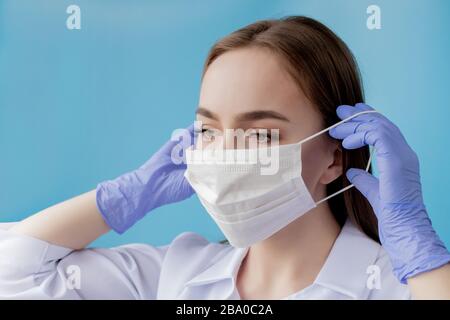 Infirmière du médecin souriant derrière le masque du chirurgien. Gros plan portrait de la jeune femme caucasienne modèle sur fond bleu. Femme portant une masse pour protéger le covid-19 Banque D'Images