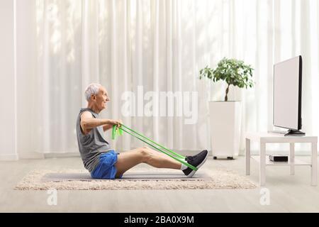 Homme âgé exerçant avec un élastique devant un téléviseur à la maison Banque D'Images