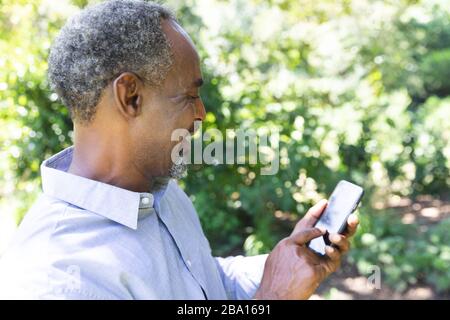 Vue latérale d'un homme d'Amérique d'Afrique de haut niveau utilisant son téléphone dans un jardin Banque D'Images