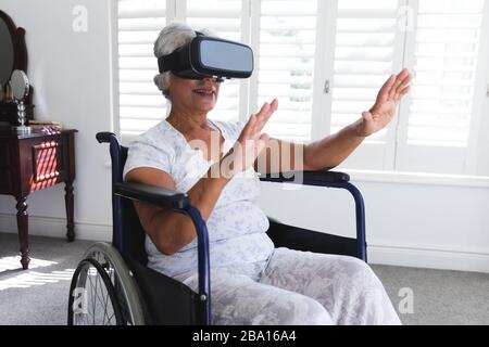 Vue latérale d'une femme afro-américaine âgée assise dans un fauteuil roulant et utilisant la réalité virtuelle Banque D'Images