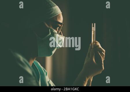 Photographie conceptuelle d'un médecin tenant et regardant un tube à essai tout en testant des échantillons pour la présence de coronavirus (COVID-19). Banque D'Images