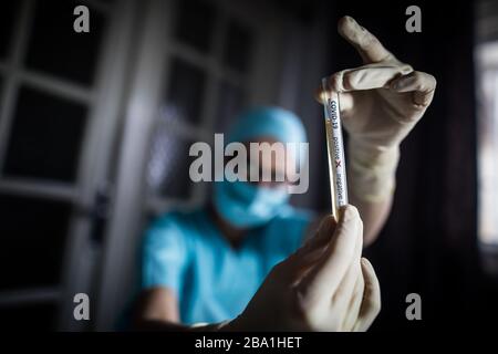 Photographie conceptuelle des mains d'un médecin tenant et regardant un tube à essai alors qu'avec des échantillons positifs pour la présence de coronavirus (COVID-19). Banque D'Images