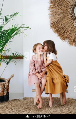 Couple de petites filles du même âge assis sur un banc, chuchotant dans l'oreille Banque D'Images