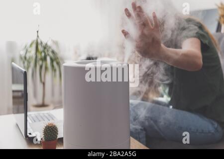 Femme indépendante utilise un humidificateur domestique sur le lieu de travail au bureau à domicile avec un ordinateur portable et des documents. Banque D'Images