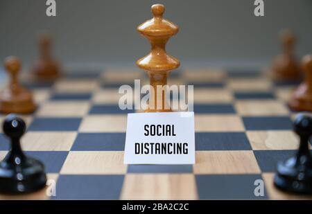Les pièces d'échecs de concept expriment l'éloignement social avec le tableau blanc et le texte social distancer devant la pièce centrale sur le tableau d'échecs. Banque D'Images