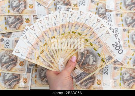 La femme tient les billets polonais sur le devant, valeur faciale 200 PLN disposés en éventail, en arrière-plan une pile de billets polonais. Banque D'Images