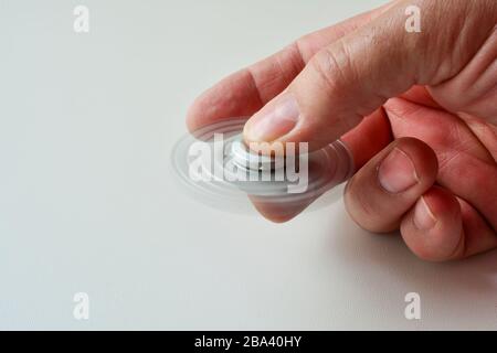 Disque de fidget couleur argent en mouvement dans la main de l'homme sur fond blanc, vue latérale, espace de copie sur la gauche Banque D'Images