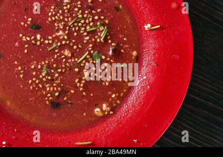 Restes de salade après le repas. Huile, graines de tomate, persil haché sur une seule plaque rouge. Gros plan Banque D'Images