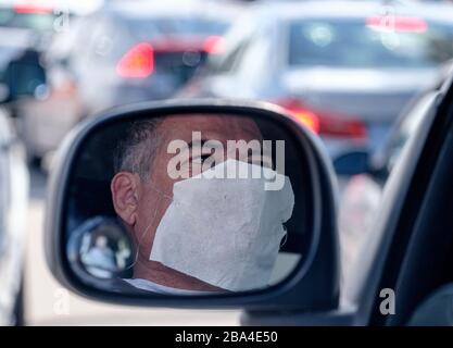 Los Angeles, Californie, États-Unis. 24 mars 2020. Steve Oliveira, 58 ans, portant un masque facial se reflète dans le rétroviseur de son véhicule alors qu'il attend dans son véhicule doublé à l'extérieur du Centre chrétien de Crenshaw pour COVID-19 dans le sud de Los Angeles, le mercredi 25 mars 2020. Gov de Californie. Gavin Newsom a publié jeudi un ordre de séjour à domicile à l'échelle de l'État pour que les résidents s'aventurant à l'extérieur seulement pour des emplois essentiels, des errands et un certain exercice, en raison des préoccupations de coronavirus. Crédit: Ringo Chiu/ZUMA Wire/Alay Live News Banque D'Images