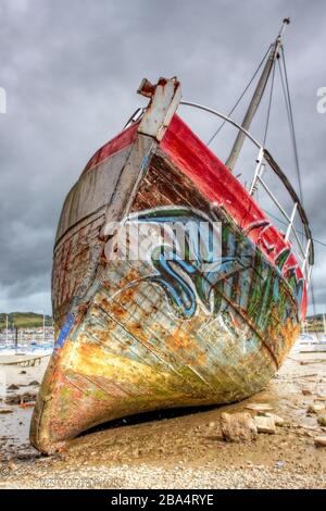 Vieux bateau abandonné sur la rive de la rivière, couvert de graffitis Banque D'Images