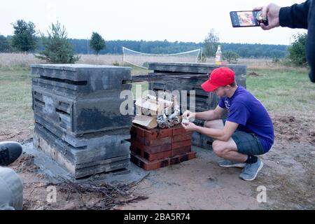 Un jeune homme allume un feu dans la nouvelle cheminée extérieure qu'il a aidé à concevoir et à construire. Zawady Gmina Rzeczyca Pologne Banque D'Images