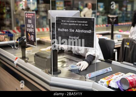 Duderstadt, Allemagne. 25 mars 2020. Un employé d'un marché d'Edeka est assis au comptoir-caisse derrière un garde-broche. Les mesures visant à contenir le coronavirus affectent massivement la vie publique en Basse-Saxe. Crédit: Swen Pförtner/dpa/Alay Live News Banque D'Images