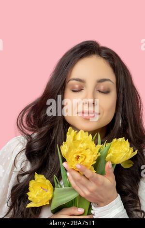 Jeune femme à poil sombre qui tient des fleurs jaunes et les sent Banque D'Images