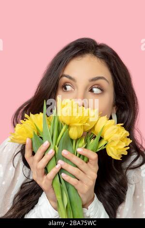 Jeune femme à poil sombre qui tient des fleurs jaunes et qui a l'air surprise Banque D'Images