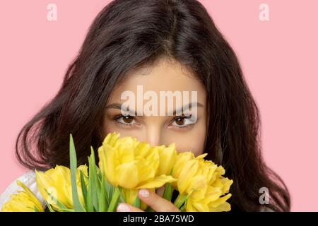 Jeune femme à poil sombre qui cache le visage dans les fleurs Banque D'Images