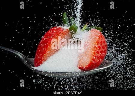 Fraise fraîche en deux sur une cuillère avec une pile de saupoudrer de sucre blanc. Concept de sucres cachés dans les fruits Banque D'Images