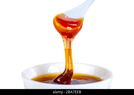 le miel s'écoule de la cuillère en céramique à la cuvette en céramique Banque D'Images